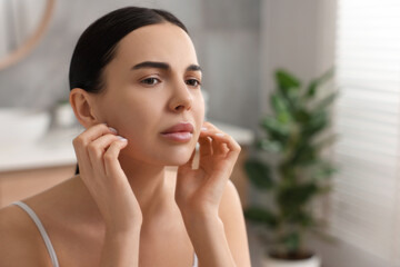 Wall Mural - Woman with dry skin checking her face near mirror indoors, space for text