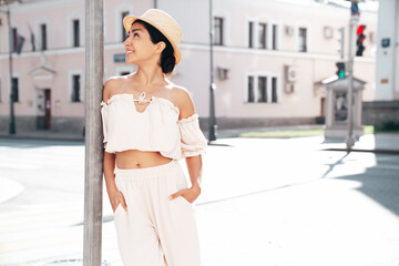 Young beautiful smiling hipster woman in trendy summer costume clothes. Carefree female posing in the street at sunny day. Positive model outdoors at sunset. Cheerful and happy in hat