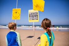 Kids Checking The Beach Report Sign At The Beach