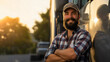 © Nemanja - A professional male truck driver, wearing a shirt and a hat, standing with his arms crossed in front of the truck on the road, and smiling at the camera. Trucking transportation job worker, happy man