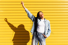 Woman with hand raised standing in front of corrugated shutter on sunny day