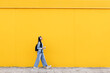 © VISTA by Westend61 - Young woman walking on footpath in front of yellow wall