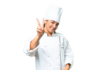 Wall Mural - Young woman Chef over isolated chroma key background smiling and showing victory sign