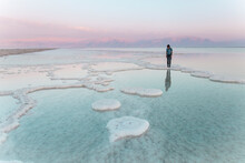 Young Woman Standing On Salt Formations In Dead Sea At Sunset