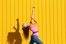 Young Woman Wearing Bodysuit Dancing In Front Of Yellow Wall