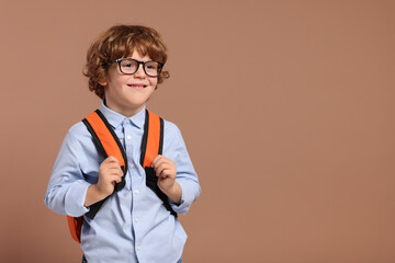 Happy schoolboy in glasses with backpack on brown background, space for text