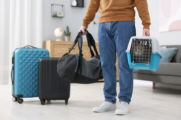 Sticker - Travel with pet. Man holding carrier with cute cat and bag at home, closeup