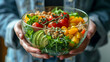 The hands of a young woman hold a transparent bowl with a salad of fresh tomatoes, avocado, yellow sweet pepper and green leaves. A delicious and balanced diet, proper nutrition, vegan food.
