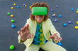© VISTA by Westend61 - Woman wearing green VR glasses sitting amidst colorful balls on terrace
