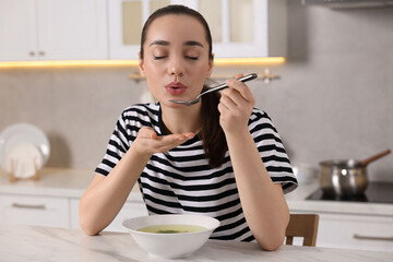 Wall Mural - Beautiful woman eating tasty soup at white table in kitchen