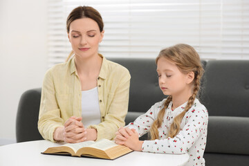 Wall Mural - Girl and her godparent praying over Bible together at table indoors