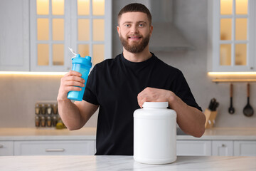 Poster - Young man with shaker of protein and powder at white marble table in kitchen