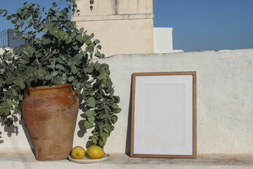 Wall Mural - Empty vertical wooden frame picture mockup against white old textured white wall in sunlight. Fresh yellow lemons fruit, old vase with eucalyptus. Summer background, Mediterranean design.