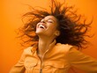 woman with dreadlocks stands confidently in front of a vibrant orange background.