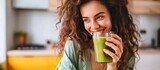 Fototapeta  - Happy young woman drinking a glass fresh green healthy smoothie at home. AI generated