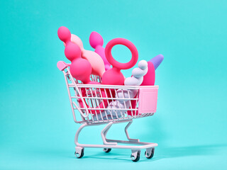 Wall Mural - Female pink sex toys in shopping trolley over turquoise background