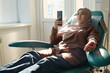 Muslim woman relaxing on medical chair and scrolling smartphone during blood transfusion in hospital