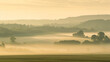 A hazy summer morning with gentle light filtering through the mist over a rolling countryside.