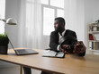 © SHOTPRIME STUDIO - An African-American man sits at his desk in front of his laptop, wearing headphones and chatting on a video call, listening to music. The concept of student business training and online work.