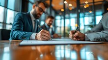 Two Businessmen Sign An Agreement In The Office. Blurred Background Of Modern Office From Behind