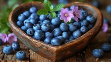  a wooden bowl filled with blueberries and a purple flower on top of a wooden table next to other blueberries and a purple flower in the center of the bowl.