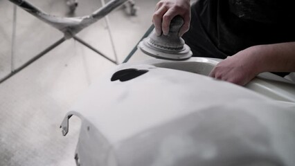 Wall Mural - A worker professionally cleans the surface of a car bumper with a grinding machine in a car service garage before painting, close-up. Sanding a car bumper before painting.