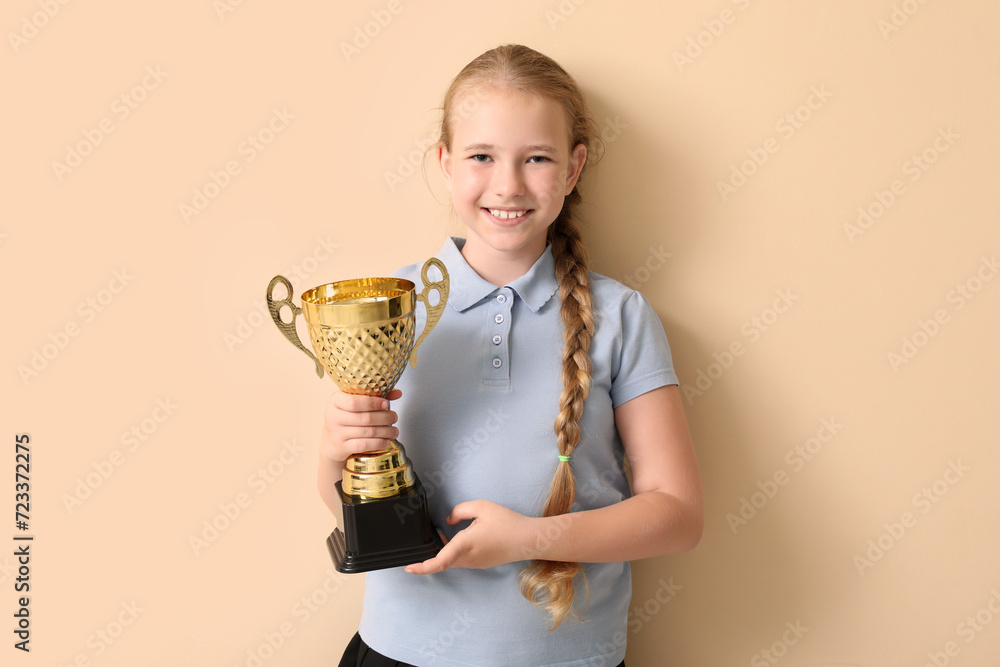 Cute little schoolgirl with gold cup on beige background