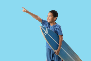 Poster - Cute little African-American boy with surfboard pointing somewhere on blue background