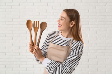 Sticker - Pretty young woman in apron with wooden utensils on white brick wall background