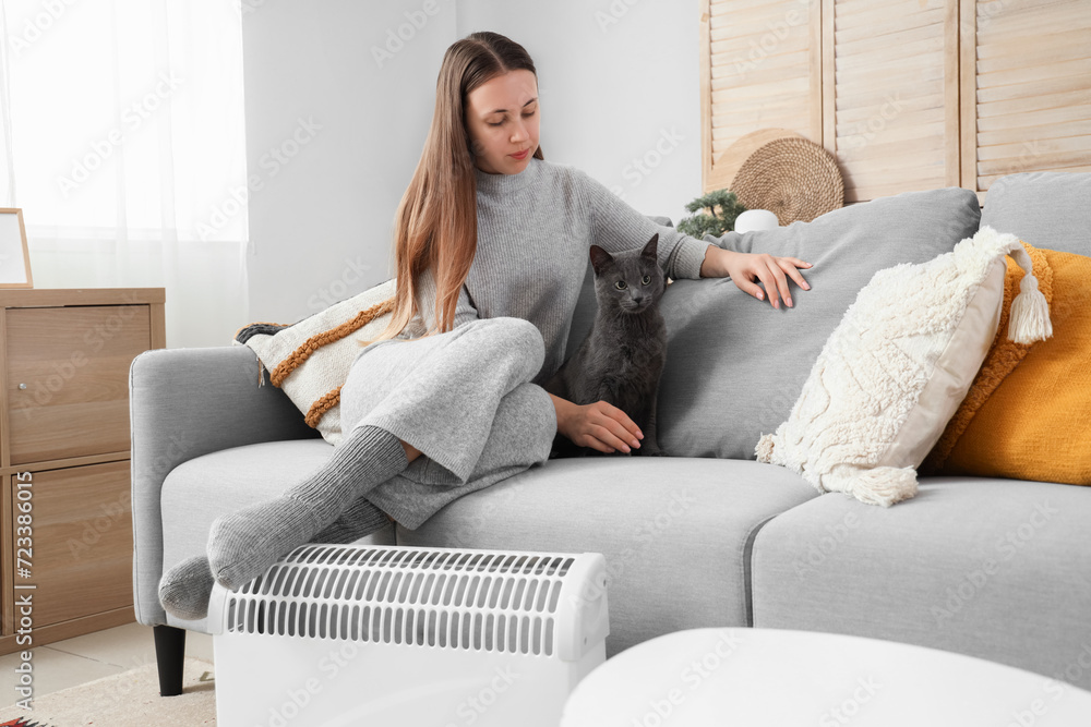 Young woman with cute cat and radiator at home
