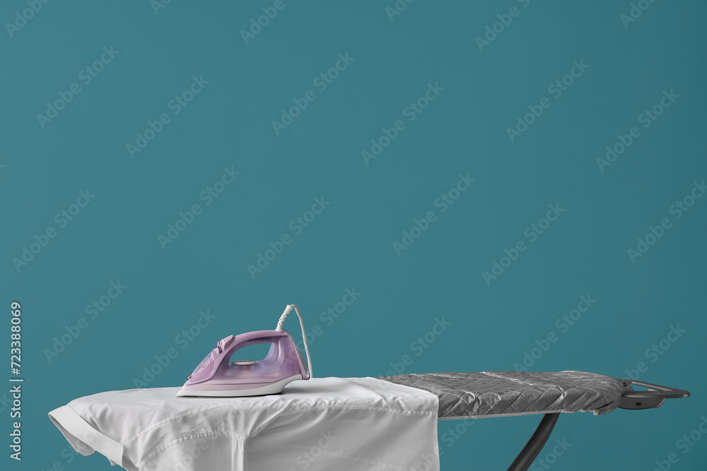 Electric iron with white shirt on board against blue background