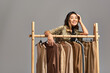 © LIGHTFIELD STUDIOS - cheerful asian stylist smiling at camera near rack with bespoke clothes on grey, fashion business