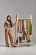© LIGHTFIELD STUDIOS - cheerful asian designer with measuring tape near rack with trendy clothes on grey backdrop