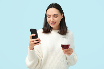 Poster - Beautiful young woman with glass of red wine and mobile phone on blue background