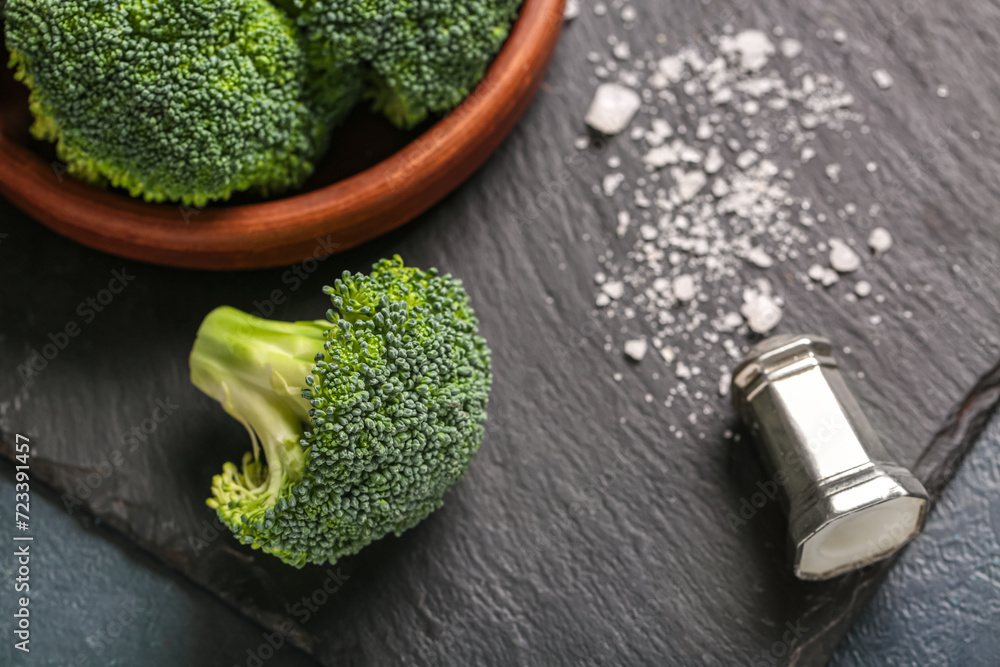 Bowl with fresh green broccoli, board and salt on black grunge background