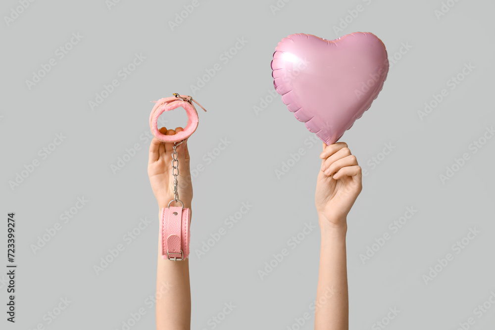 Female hands with heart shaped balloon and handcuffs on white background. Valentine's Day celebration