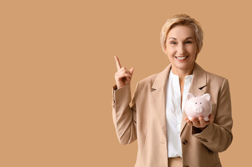 Sticker - Beautiful mature woman with piggy bank pointing at something on brown background