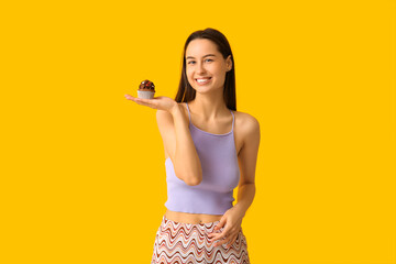 Canvas Print - Young woman with sweet cupcake on yellow background. Valentine's Day celebration