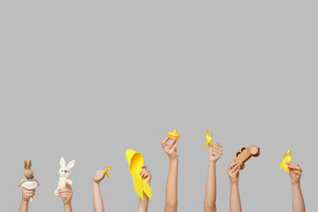 Poster - Children hands holding toys and yellow ribbons on grey background. International Childhood Cancer Day