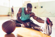 © Marko Geber - Young man stretching after playing basketball in an indoor basketball gym