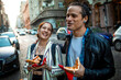 © Marko Geber - Young couple eating a slice of pizza and crossing a street in the city