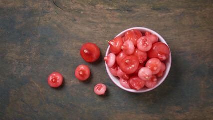 Wall Mural - jambu or rose apple, aka bell fruit or wax apple, flesh is crisp and watery, cup full of bell-like or pear shaped juicy fruits on wooden table surface, taken from above with copy space