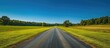 © Lasvu - In summer, a clear blue sky overlooks a verdant field with an empty road.