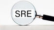 SRE. Site Reliability Engineering lettering on through a magnifying glass on a light background