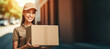 Delivery courier service. Cute woman-courier in uniform holding cardboard box in hand. Smiling femme postal against the background of blurred street.