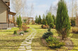 early spring garden view with stone pathway and wooden house on background