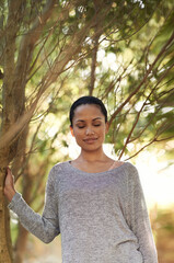 Woman, tree and eyes closed for peace in woods, travel and thinking about life, mindfulness and sunshine. Forest, nature and calm outdoor, zen and dream in environment with tranquility and fresh air