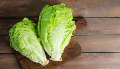 Wall Mural - Iceberg lettuce on cutting board on wooden table background, top view. Two whole heads of fresh crisphead lettuce. Leafy green vegetable, selective focus