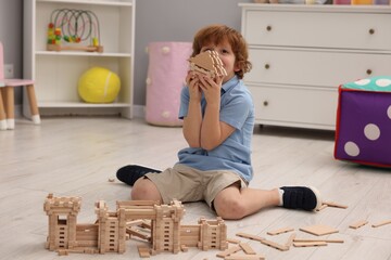 Sticker - Little boy playing with wooden construction set on floor in room. Child's toy