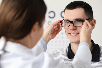 Canvas Print - Vision testing. Ophthalmologist giving glasses to young man indoors